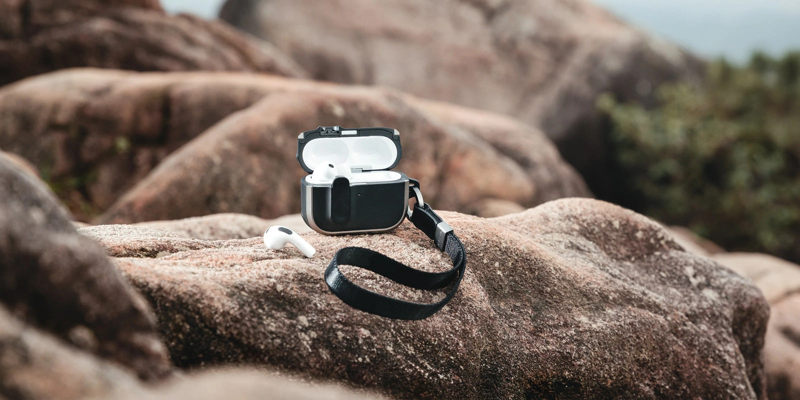 MAGEASY Odyssey rugged AirPods Pro 3 case on a rock with wrist strap attached and AirPods displayed